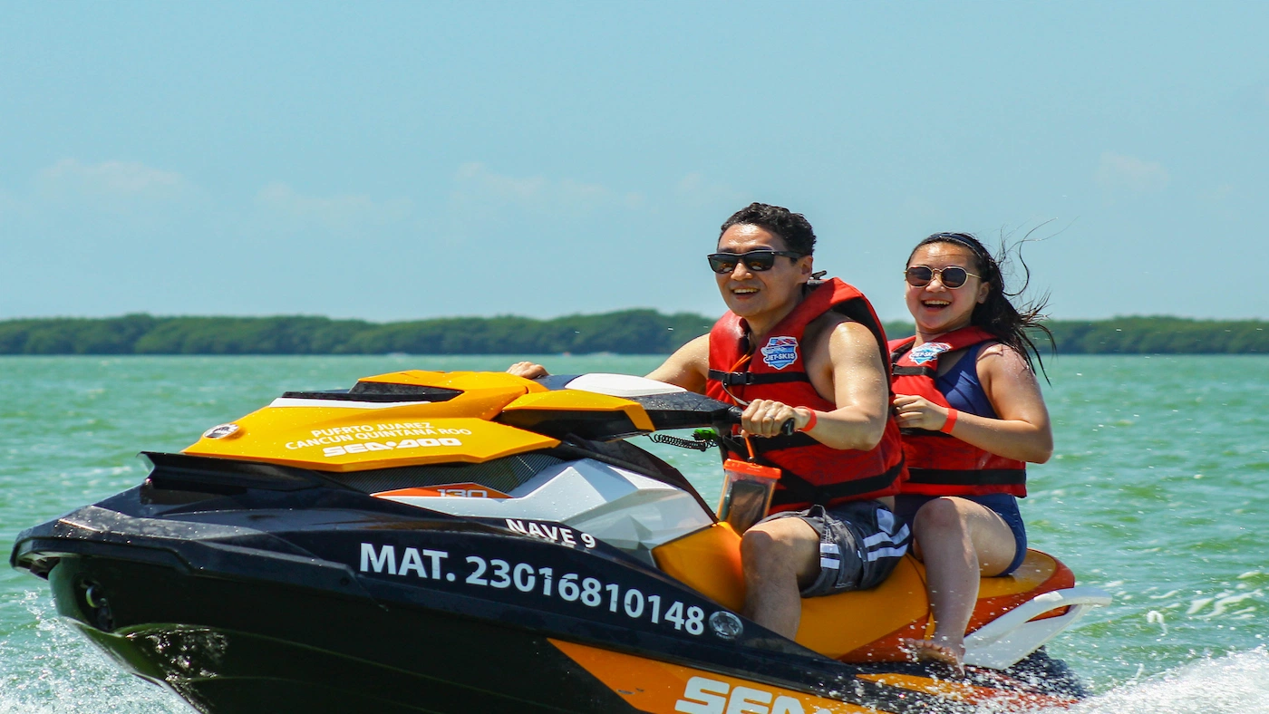 An Asian couple is riding a rented jet ski in the Cancun lagoon.